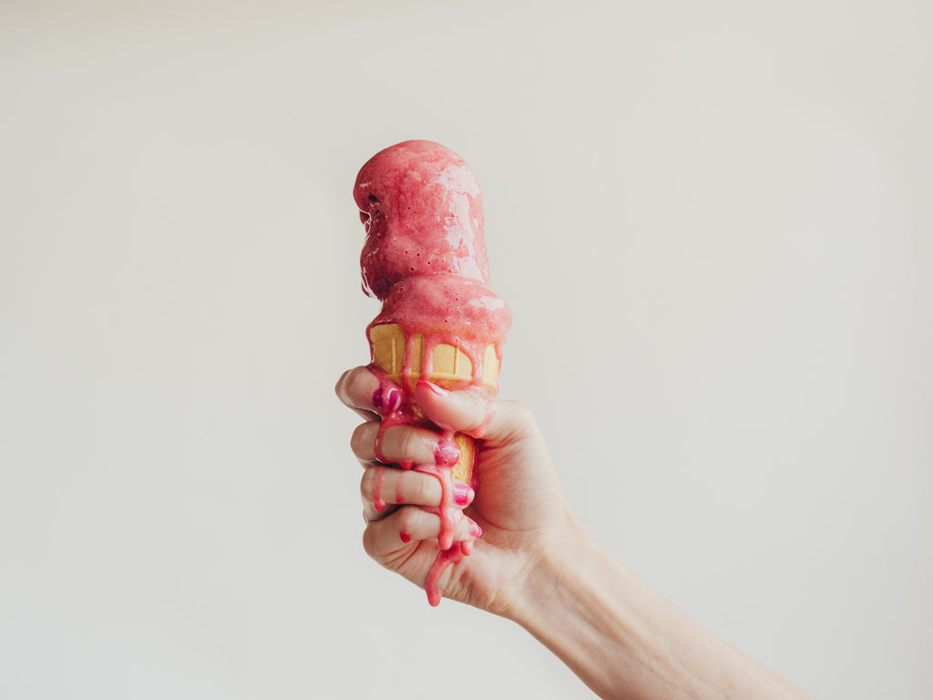 Hand holding melting strawberry ice cream in cone
